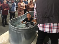 a man is being baptized in a tub in front of a group of people