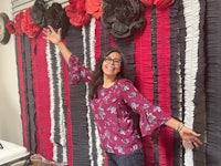 a woman is standing in front of a red and black pom pom wall