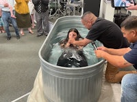 a woman is being baptized in a tub in front of a group of people
