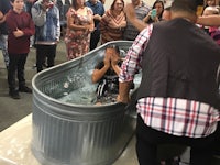 a man is being baptized in a tub in front of a group of people