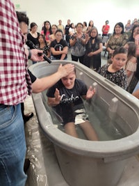 a man is being baptized in a bathtub in front of a group of people