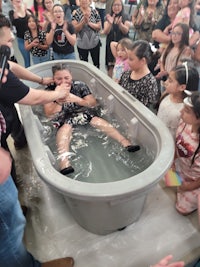 a man is being baptized in a bathtub in front of a crowd of people