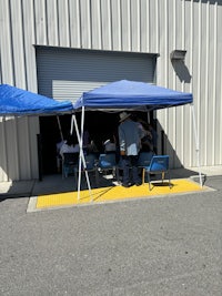a group of people sitting under a blue tent in front of a building