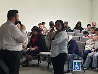 a man is speaking to a group of people in a room