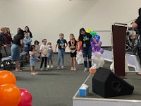 a group of children standing in front of a stage with balloons