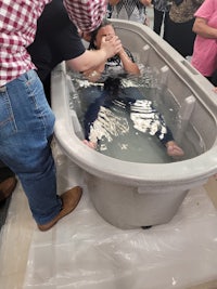 a person being baptized in a bathtub with a group of people