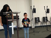 a woman standing at a podium with a boy standing next to her