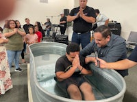 a man is being baptized in a tub in front of a group of people