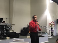 a man in a red shirt standing in front of a microphone